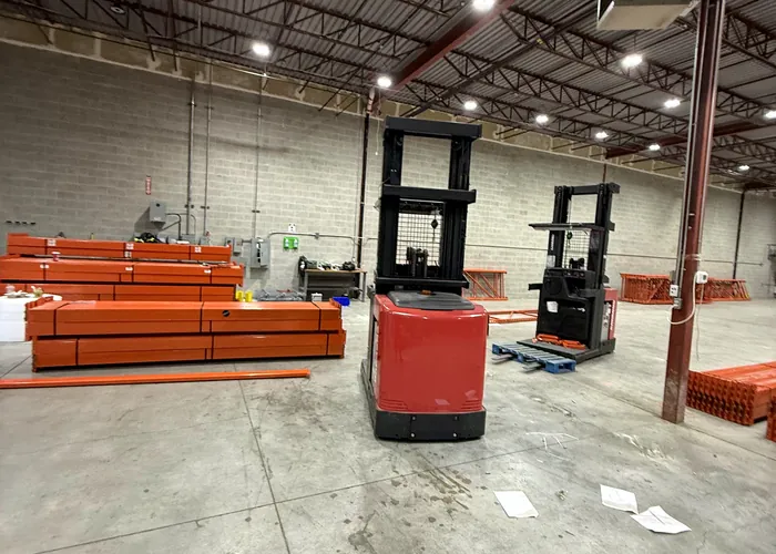 Stacks of orange beams and two order pickers on a cleared warehouse floor, with frames laid down behind them